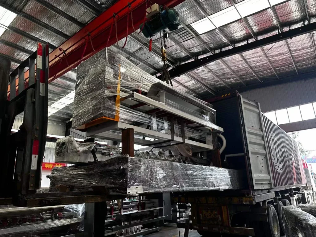 Forklift loading an automatic box stitching machine into a shipping container